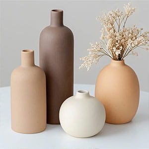 Collection of matte ceramic vases in earth tones, including beige and brown, with dried flowers on a white surface.