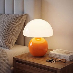 Modern orange globe table lamp with a glowing white glass shade on a wooden nightstand in a bedroom.