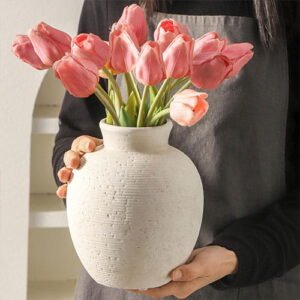 Beige textured ceramic vase filled with a bouquet of pink tulips, held by a person.