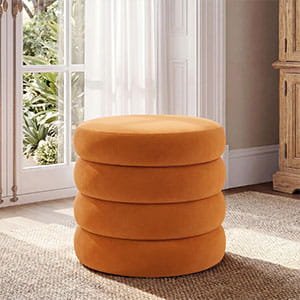 Round orange velvet pouf with a stack-like, multi-ring design in a cozy room with natural light.