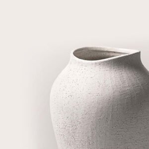 Close-up of a minimalist off-white ceramic vase with a speckled, sandy texture against a neutral background