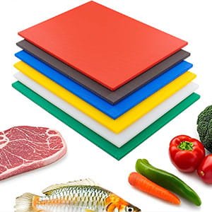 Stack of color-coded plastic cutting boards for food safety, shown with raw meat, fish, and vegetables.