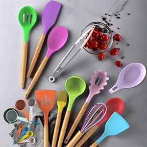 Assorted colorful silicone kitchen utensils with wooden handles, including spatulas, spoons, and a whisk, arranged on a grey surface