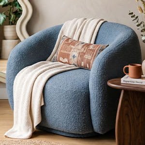 Cozy blue boucle swivel armchair draped with a white knit throw blanket, positioned in a modern minimalist living room