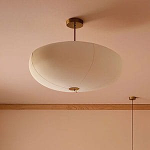 Large off-white fabric pendant light fixture with a metal base on a pinkish-beige ceiling