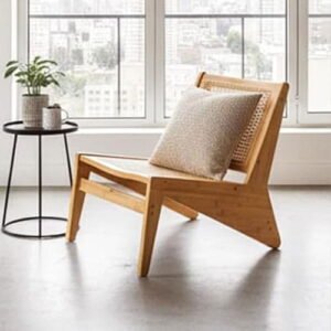 Modern natural wood lounge chair with a beige back cushion next to a black wire end table by a window.