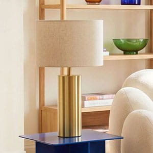 Minimalist gold cylindrical table lamp with a beige fabric shade on a blue side table
