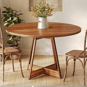 Round natural wood dining table with cross-base legs, decorated with flowers in a cozy dining room.