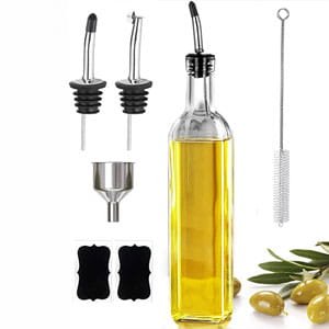 Glass olive oil dispenser bottle set with stainless steel pourers, a funnel, and cleaning brushes on a white background.