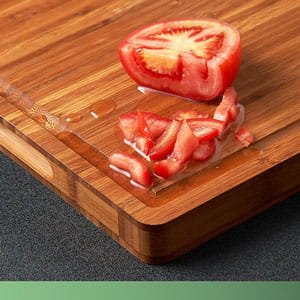 Thick wooden butcher block cutting board with a sliced tomato, showing the natural wood grain texture